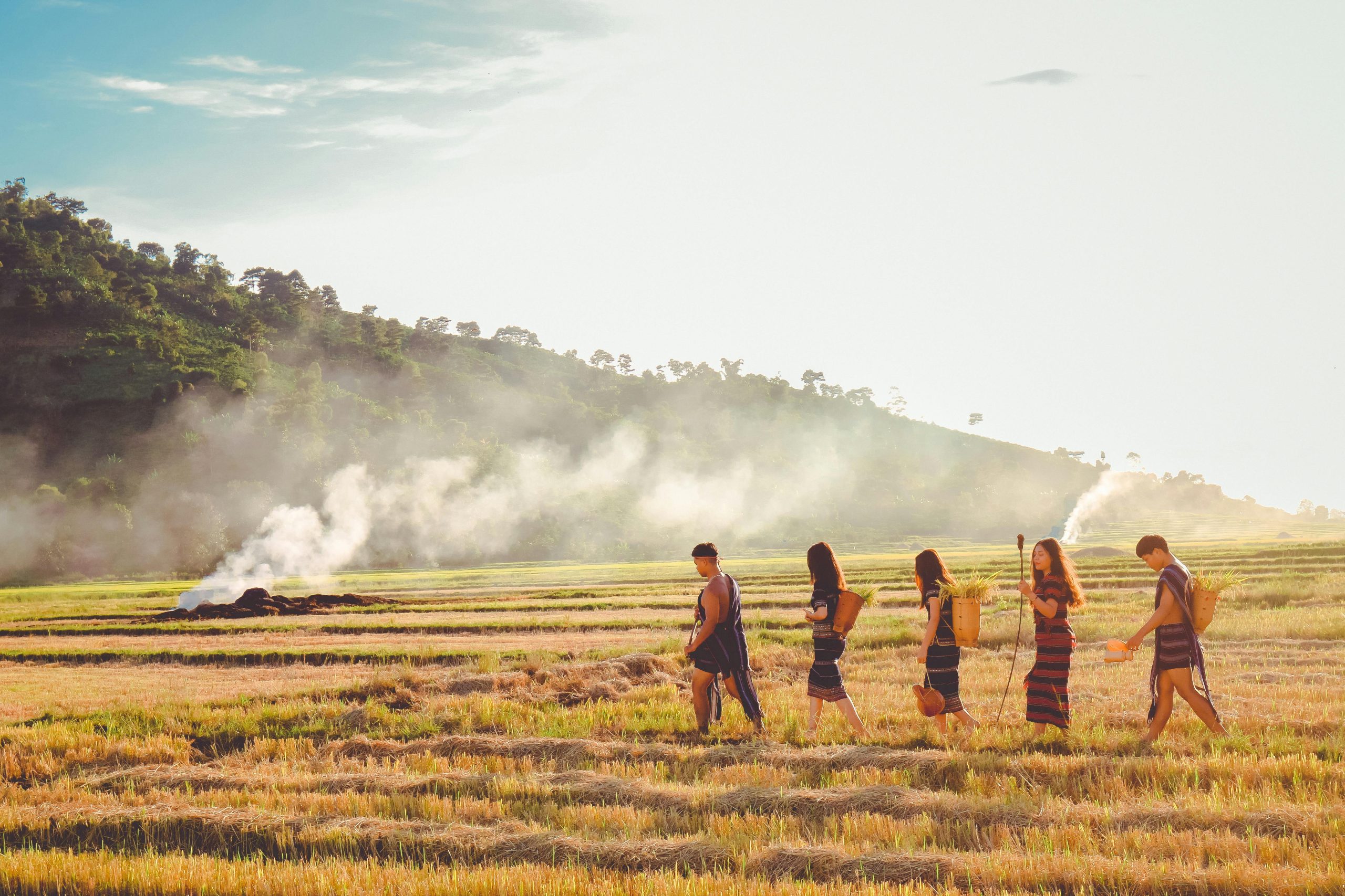 Group of people in traditional wear walking across a scenic countryside field at dawn.